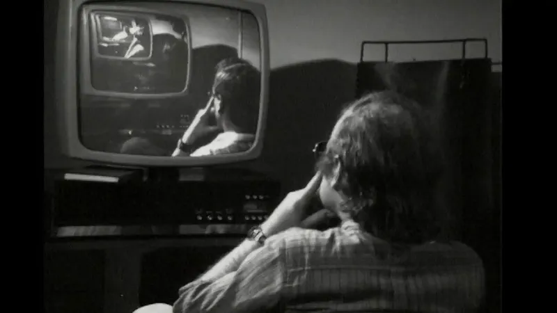 Billede fra Peter Weibels "The Endless Sandwich (Tele-Aktion I)" - der viser en 1970-agtige mand med ryggen til der kigger på et fjernsyn med ham selv set fra ryggen og videre i uendeligheden